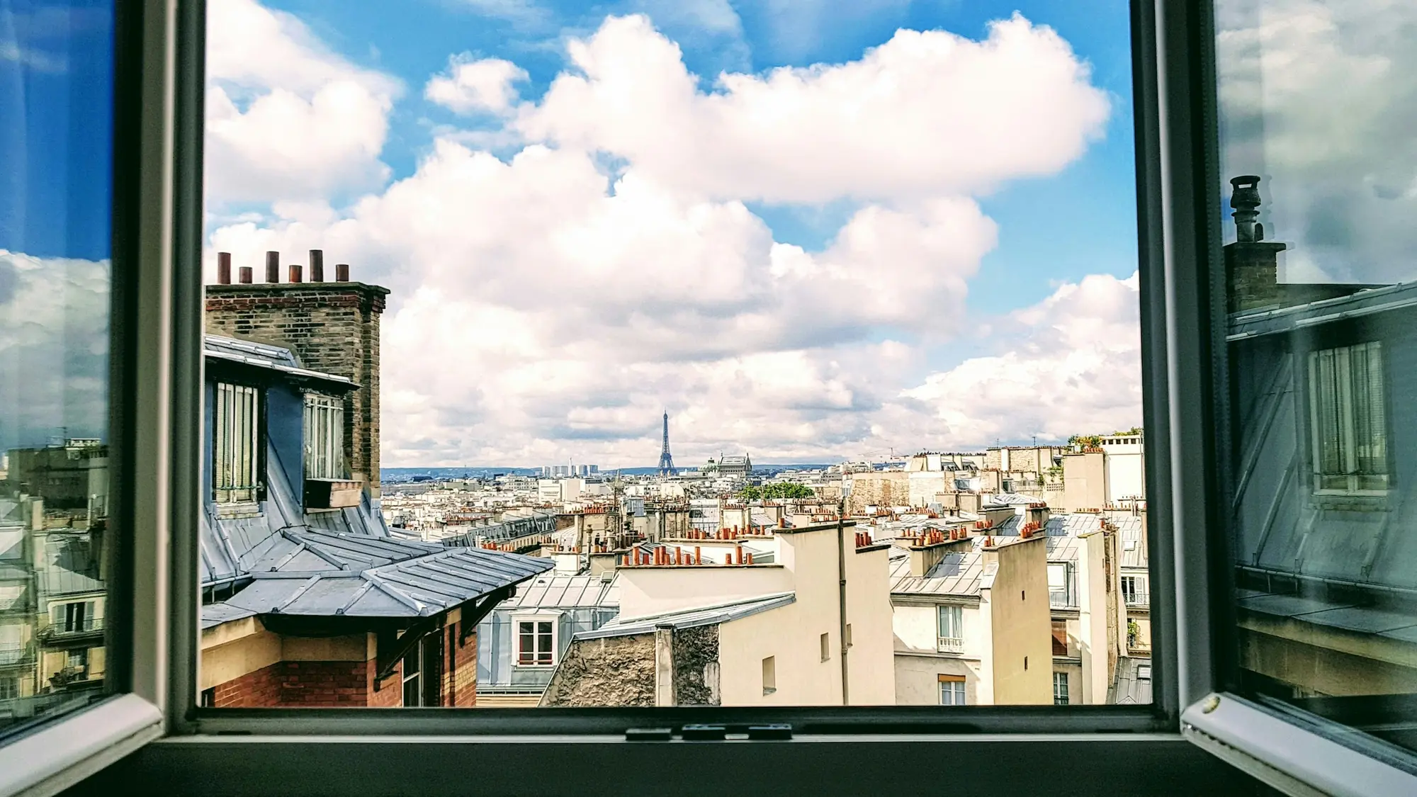 Fenêtre ouverte sur les toits de zinc de Paris, ciel bleu